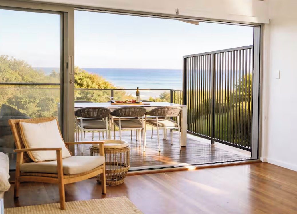 Een balkon met een tafel en stoelen, een rieten stoel en uitzicht op zee.