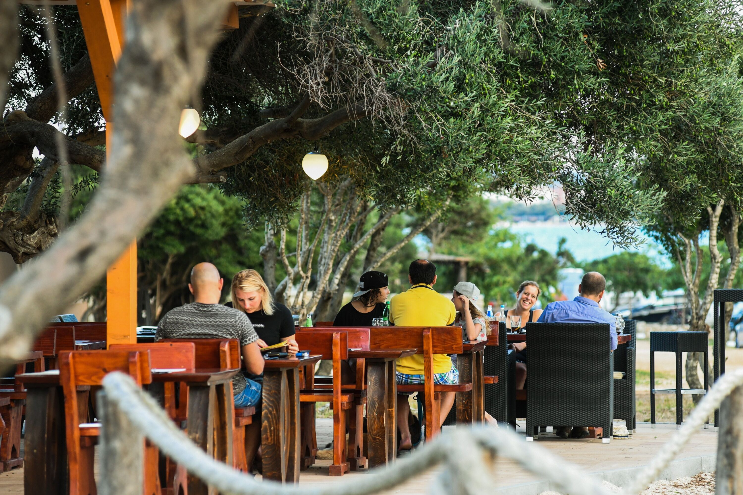 An outdoor seating area with wooden tables and chairs, surrounded by trees.