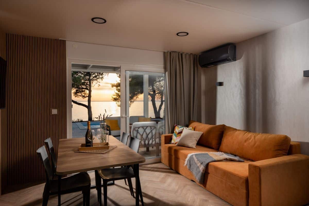 Uma sala de estar moderna com uma mesa de jantar de madeira, um sofá e vista para o exterior.