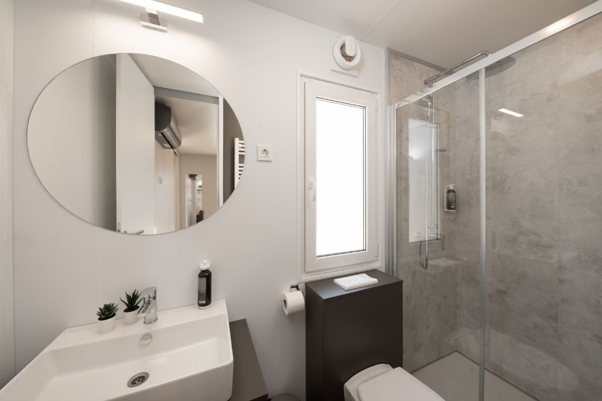 A modern bathroom with a round mirror, a sink, a toilet, and a glass-enclosed shower.