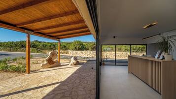A modern interior with a stone floor, a wooden reception desk, and a view of a stone wall and greenery outside.