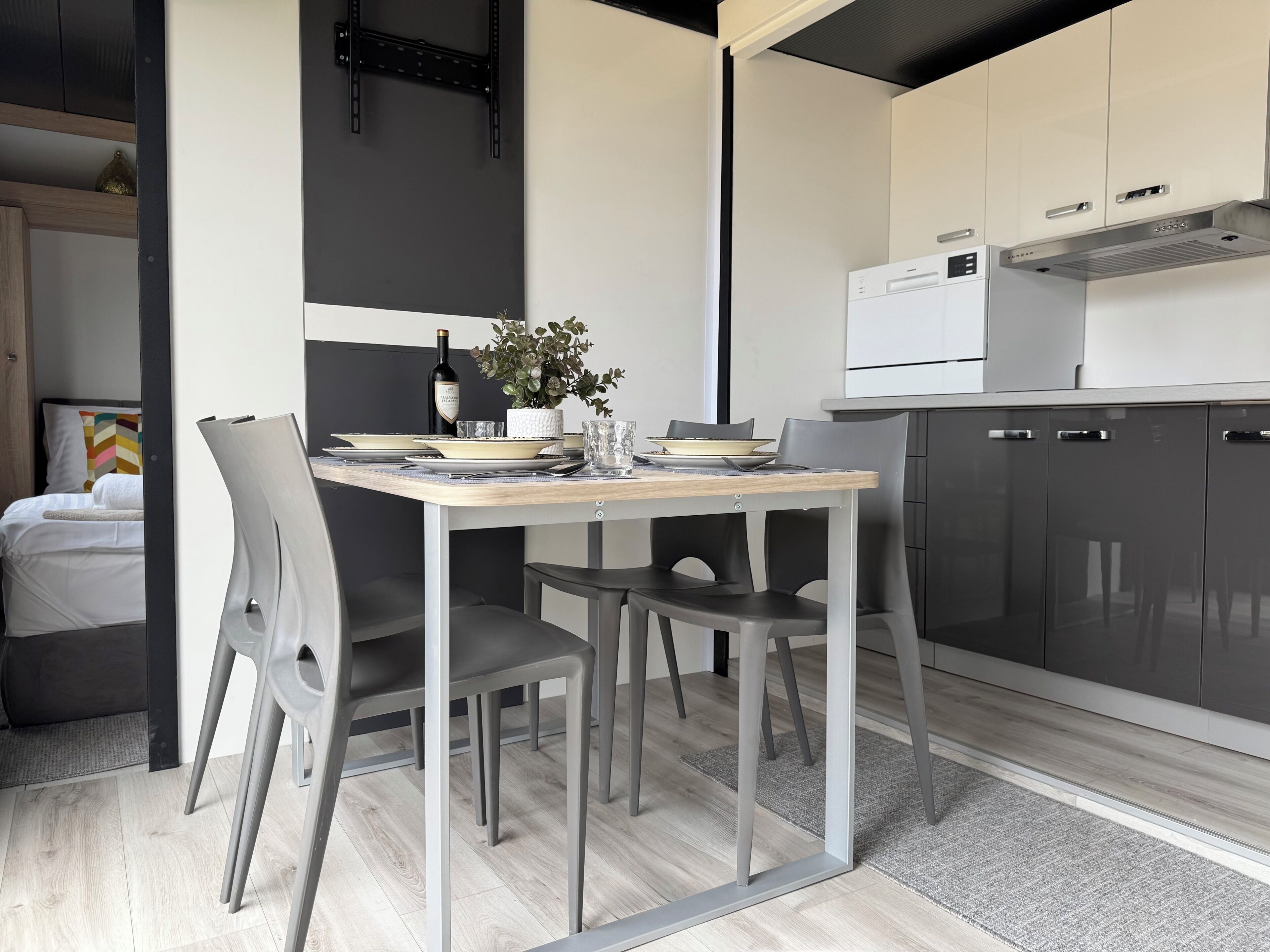 A modern kitchen with a dining table set for two, a wine bottle, and a vase of flowers.