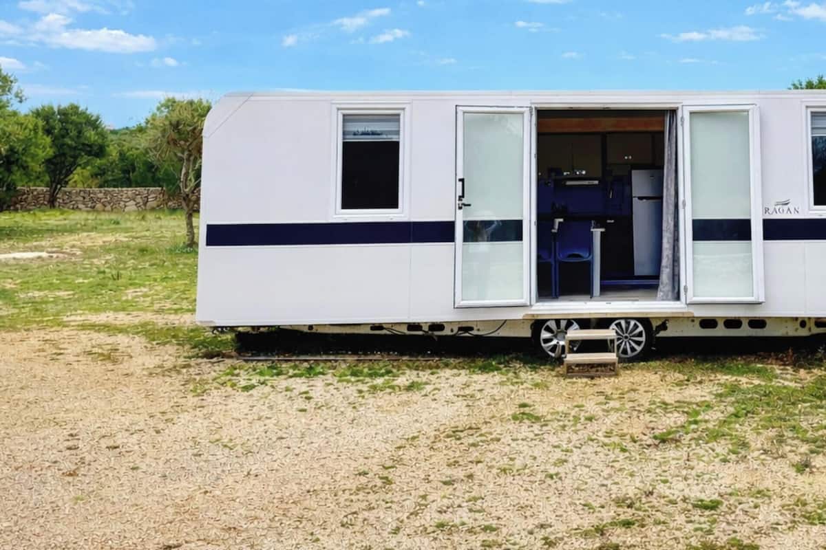 Uma casa móvel com área de cozinha visível pela porta aberta, uma pequena janela e uma porta com painel de vidro.
