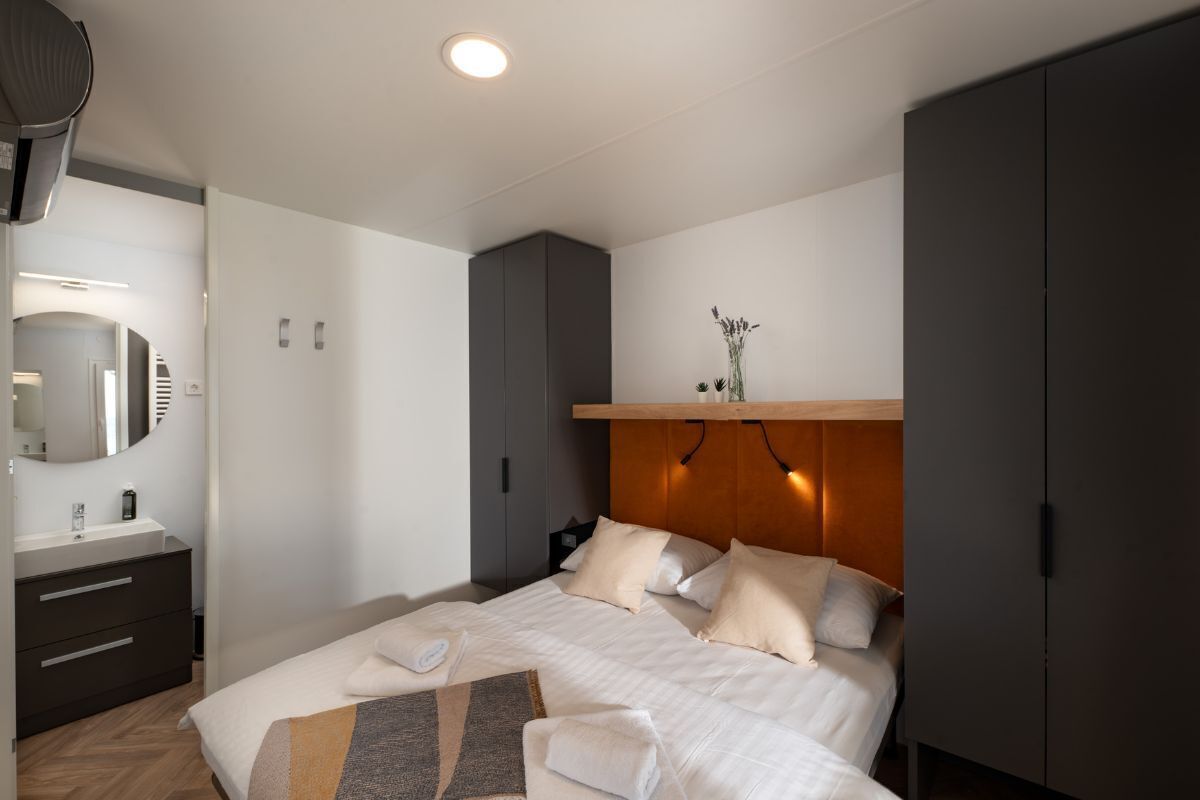 A modern hotel room with a large bed, a bedside table, a mirror, and a wardrobe.