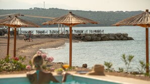 Een zwembadterras met parasols, een strand en uitzicht op zee.
