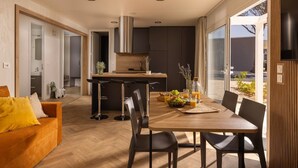 Een moderne keuken met een centraal eiland, een zithoek met een houten tafel en stoelen, en een bank met gele kussens.