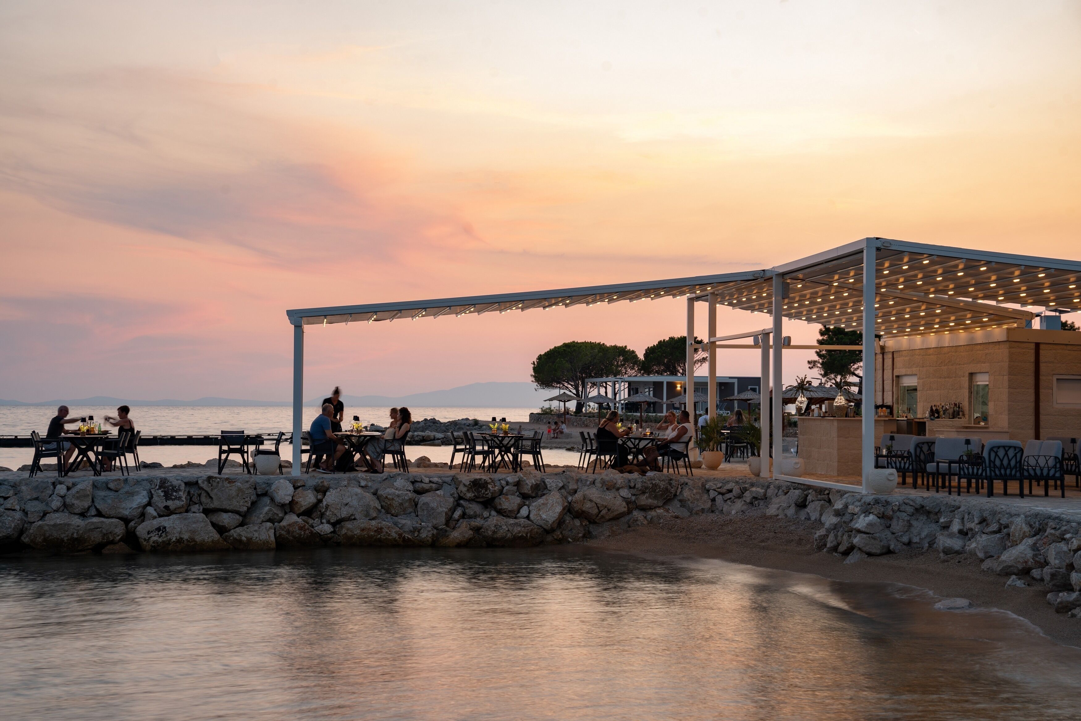 A seaside restaurant with outdoor seating, a stone wall, and a view of the sea.