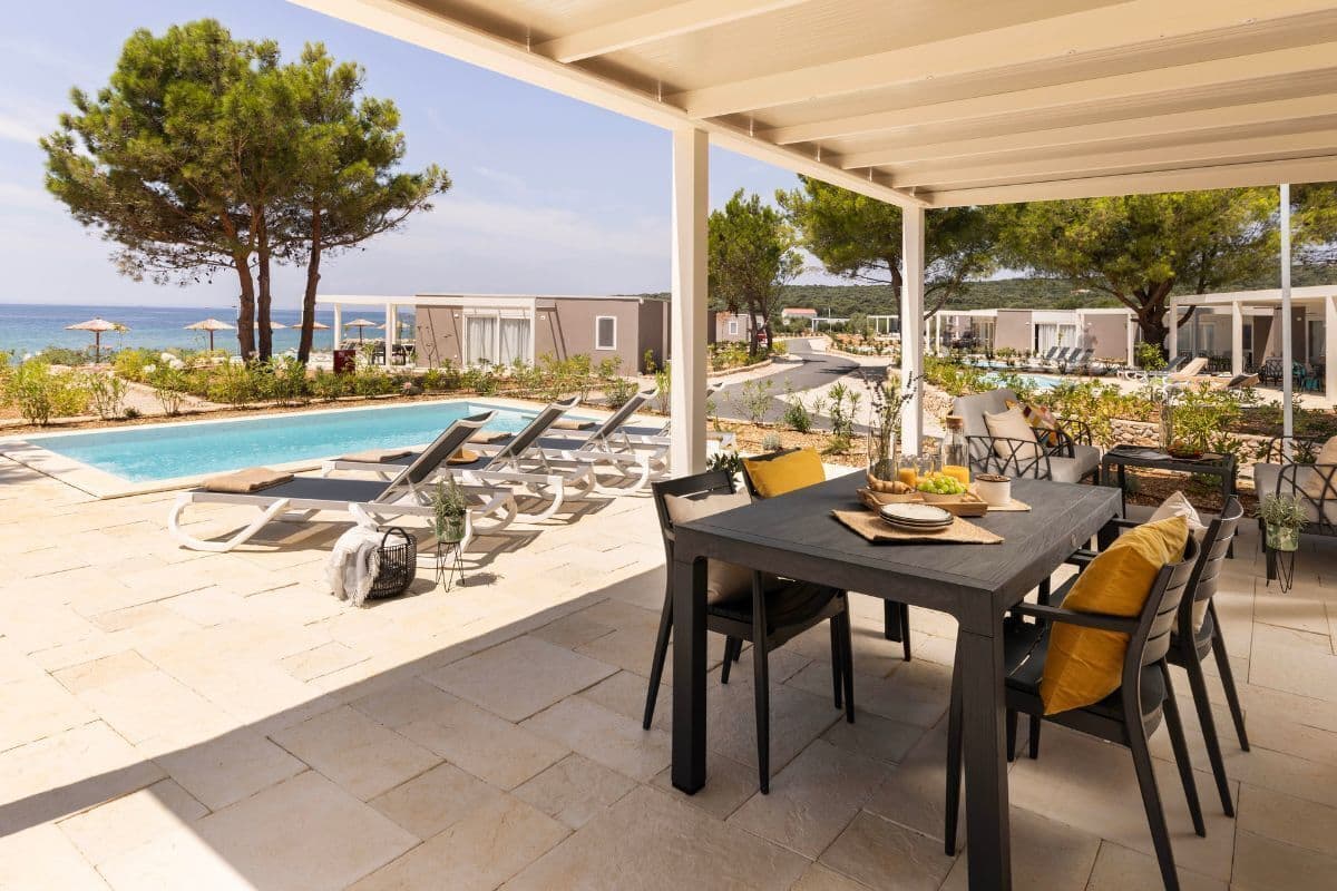 Área da piscina com espreguiçadeiras, mesa e cadeiras, e vista para o mar.