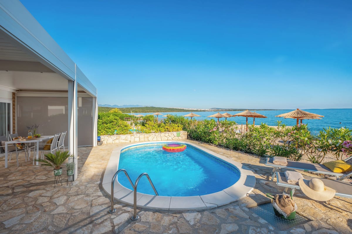 Piscina com vista para o mar, área de estar externa e um pátio de pedra.