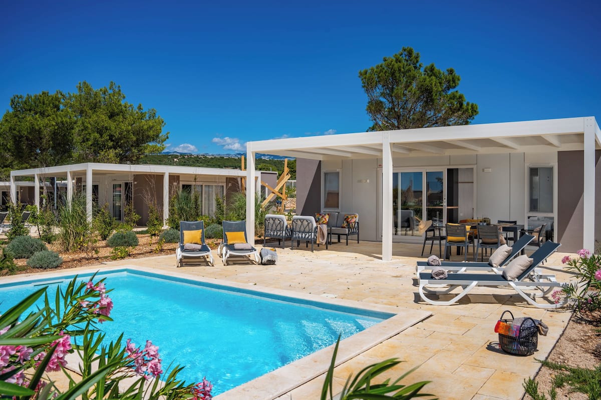 Uma área moderna com piscina ao ar livre, cadeiras de lounge e um espaço coberto para relaxar.