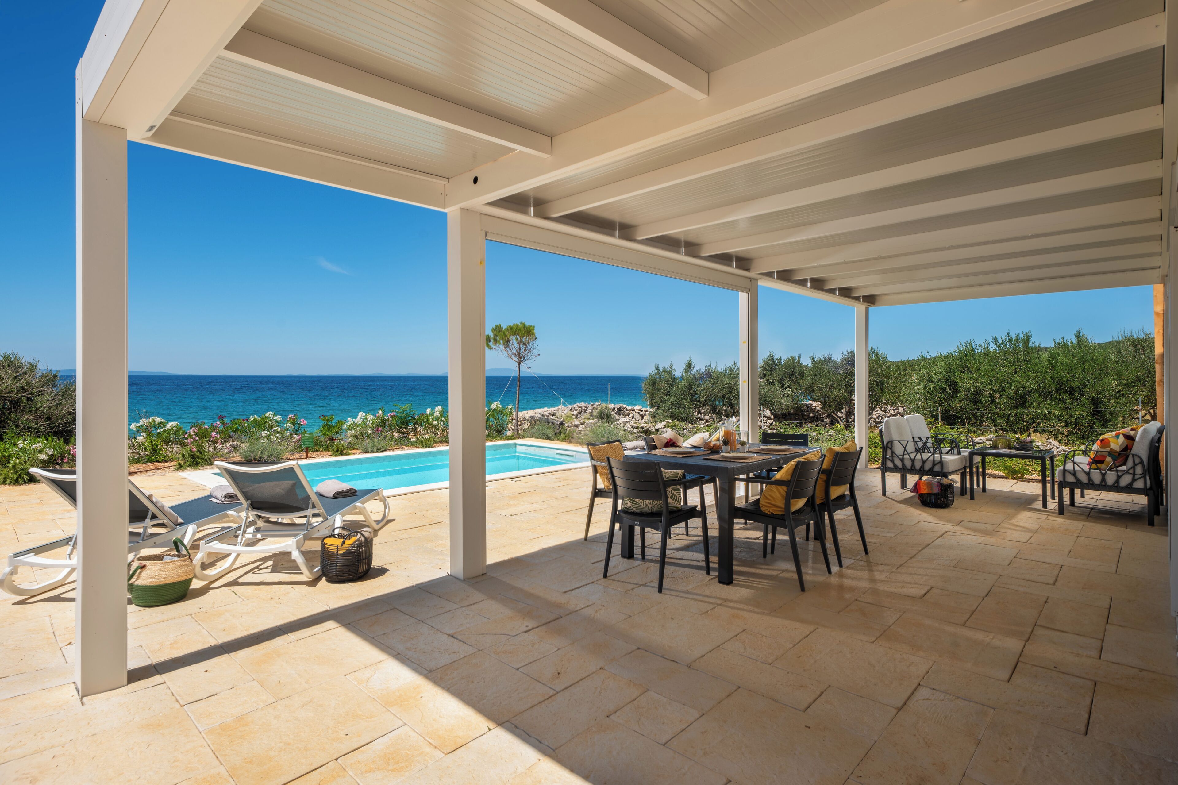 Um pátio externo com piscina, espreguiçadeiras e uma mesa com cadeiras.