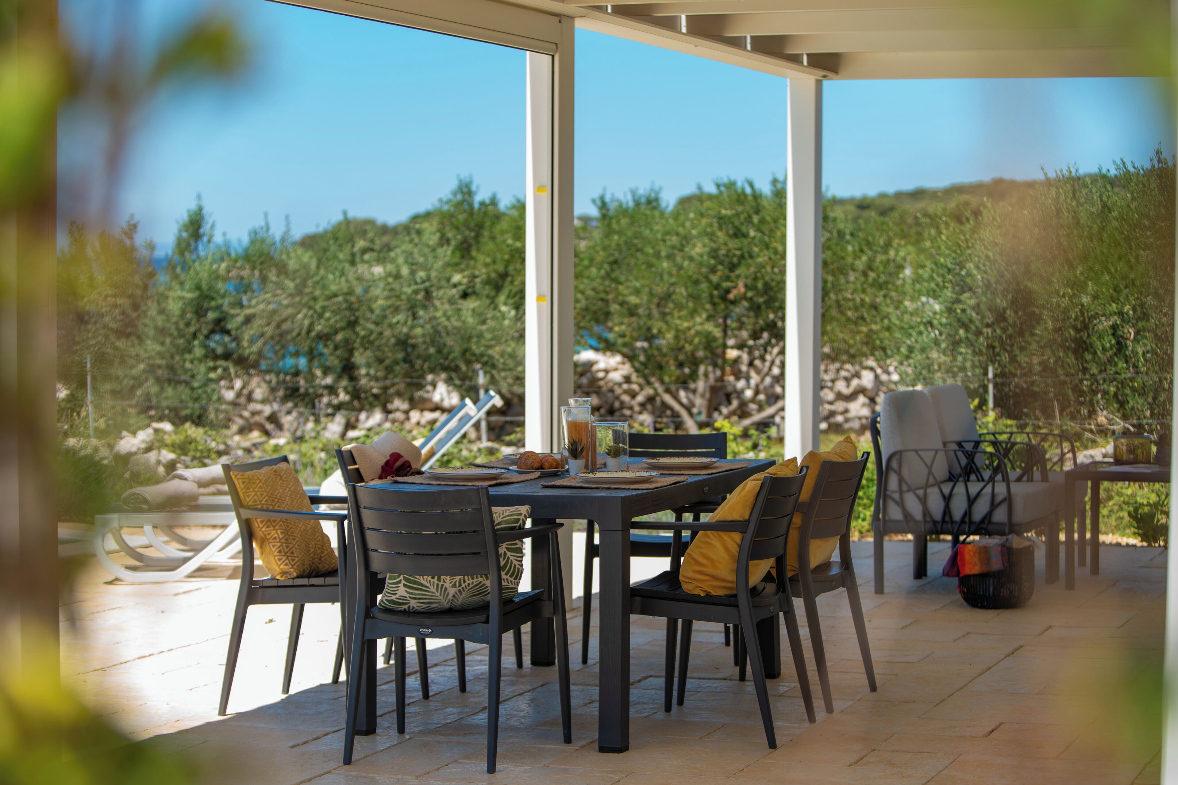Eine Terrasse im Freien mit Tisch und Stühlen, umgeben von einer natürlichen Landschaft.