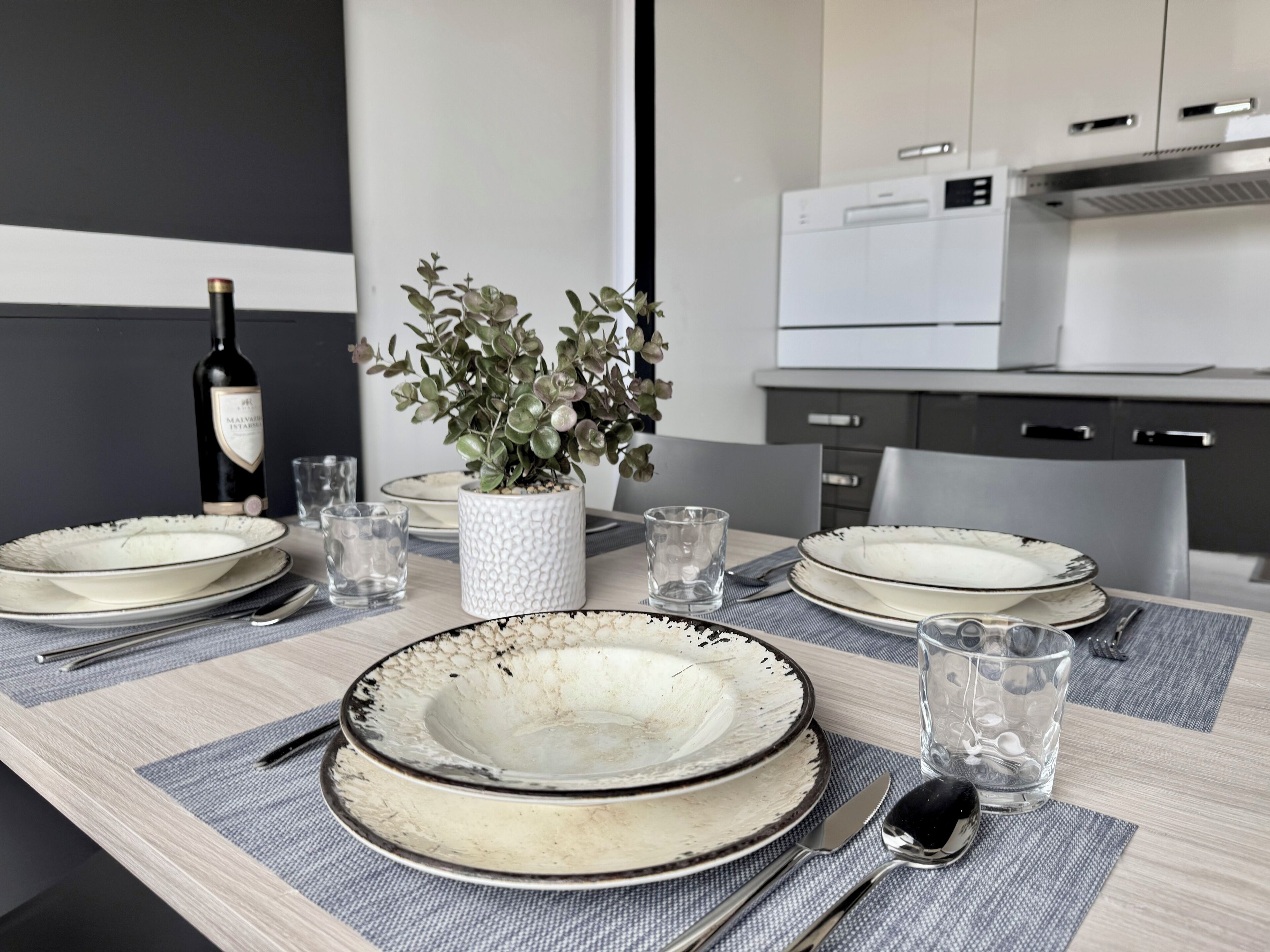 A dining table set with plates, glasses, cutlery, a bottle, and a potted plant.