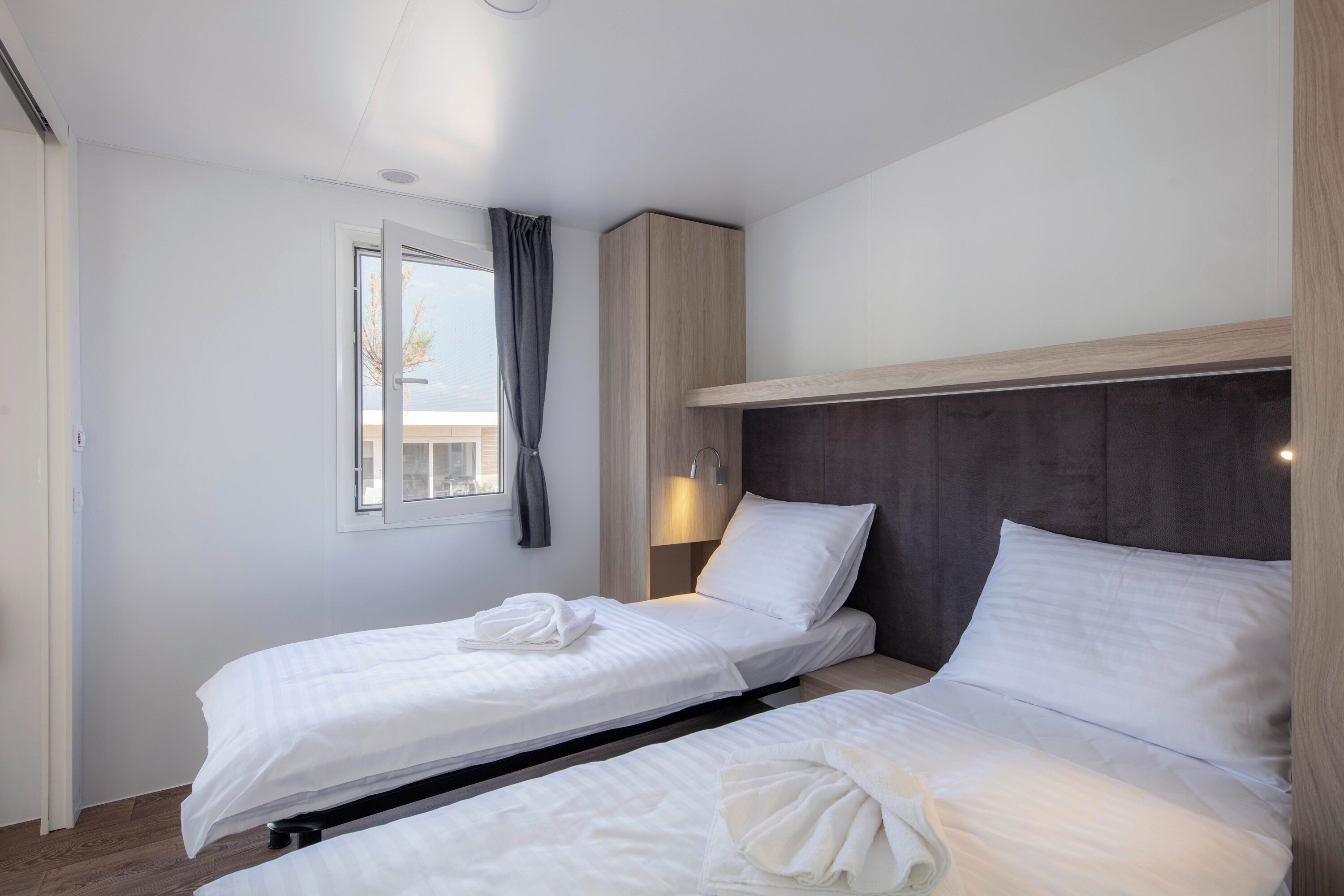 A hotel room with two single beds, a window with curtains, a bedside lamp, and a wooden headboard.