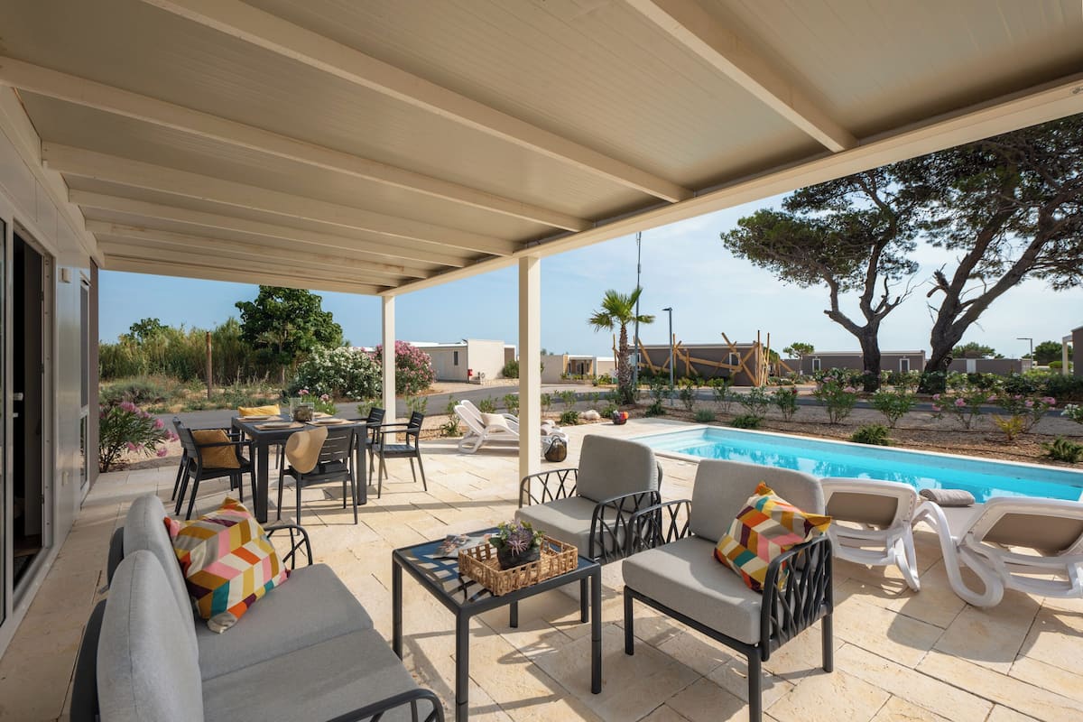 Área externa coberta com piscina, espreguiçadeiras e uma mesa com cesto e planta.