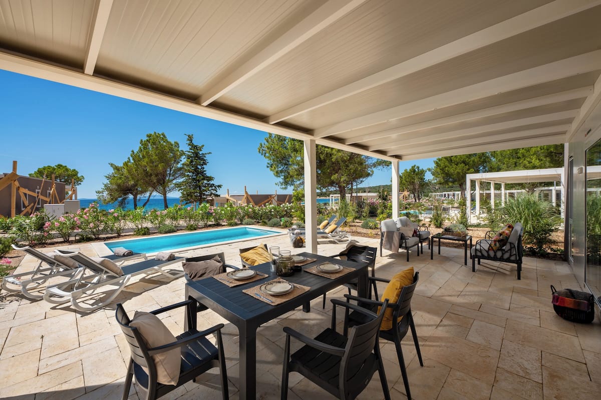 Um pátio externo com piscina, espreguiçadeiras e mesa posta para refeições.