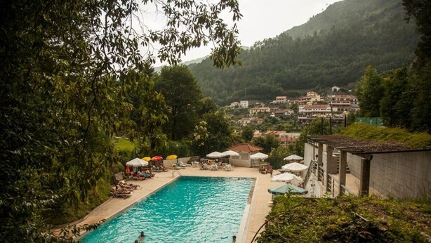 Una piscina rodeada de abundante vegetación y un pueblo en la ladera.