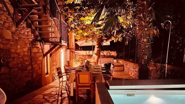 An outdoor dining area with stone walls, a pool, and a staircase leading to an upper level. - Lago Lounge & Pool Apartment in Stresa (Stresa)