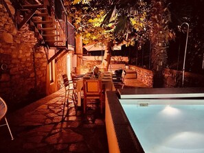 Un área de comedor al aire libre con muros de piedra, una piscina y una escalera que conduce a un nivel superior.