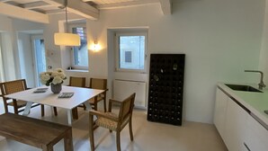 A modern kitchen with white cabinets, a wooden dining table with chairs, and a built-in wine rack. - Lago Lounge & Pool Apartment in Stresa (Stresa)