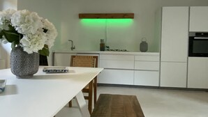 A modern kitchen with white cabinetry, a wooden bench, and a vase of white flowers on the counter. - Lago Lounge & Pool Apartment in Stresa (Stresa)