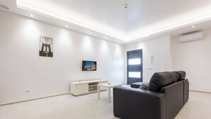 Uma sala de estar moderna com um sofá preto, um rack branco para TV e obras de arte nas paredes.