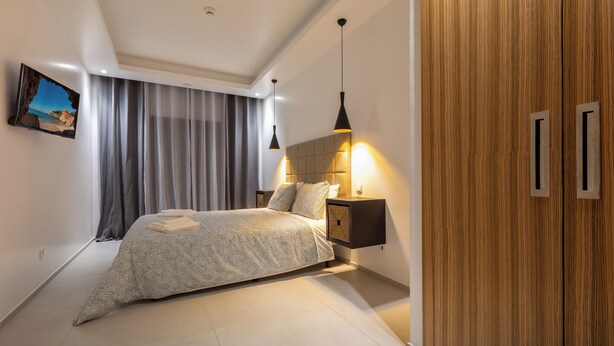 Quarto moderno com cama, mesa de cabeceira, televisão na parede e guarda-roupa de madeira.