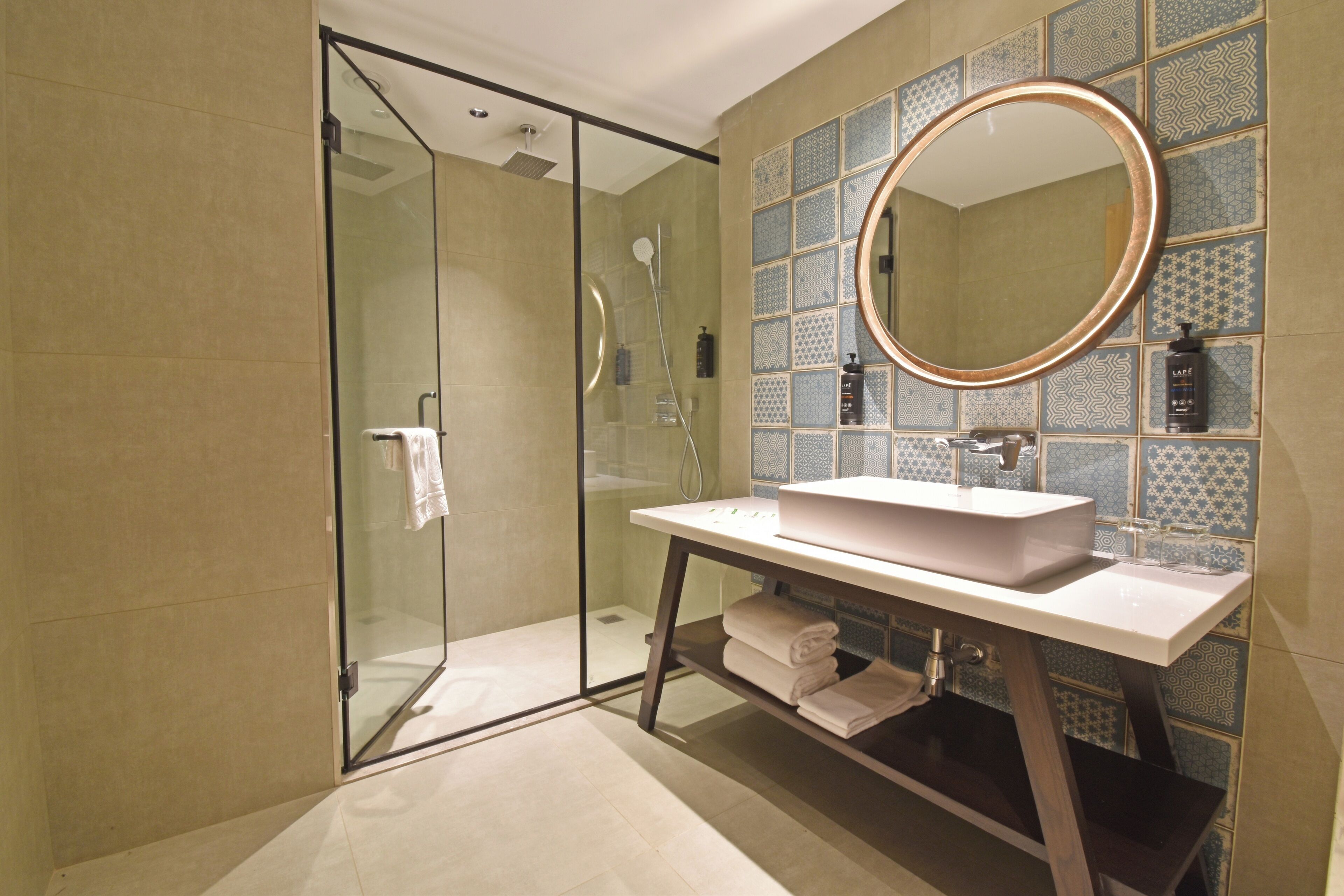 A modern bathroom with a glass shower enclosure, a white sink with a mirror, and patterned tiles on the walls.