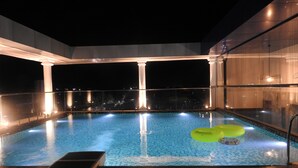 A swimming pool with a glass barrier, a green inflatable ring, and a sun lounger. - Hotel Sands Point (Puducherry)