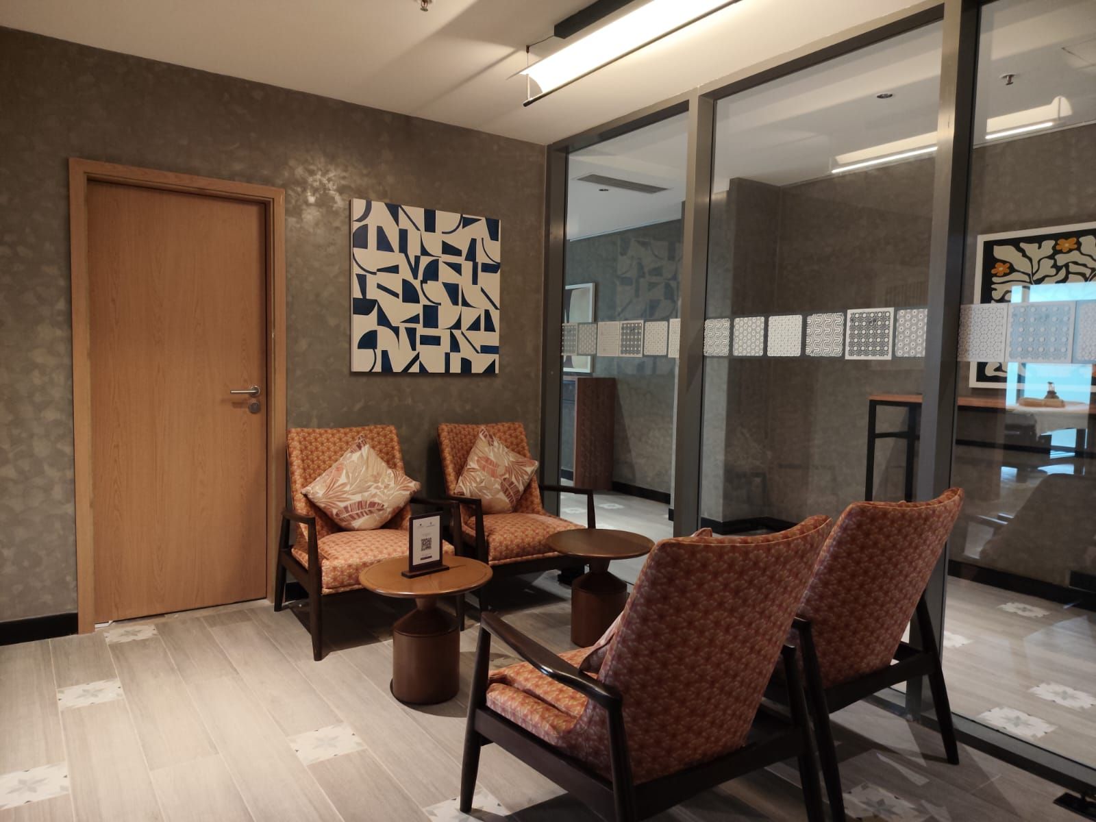 A modern interior with a wooden door, a seating area with patterned chairs, a small round table, and abstract wall art.
