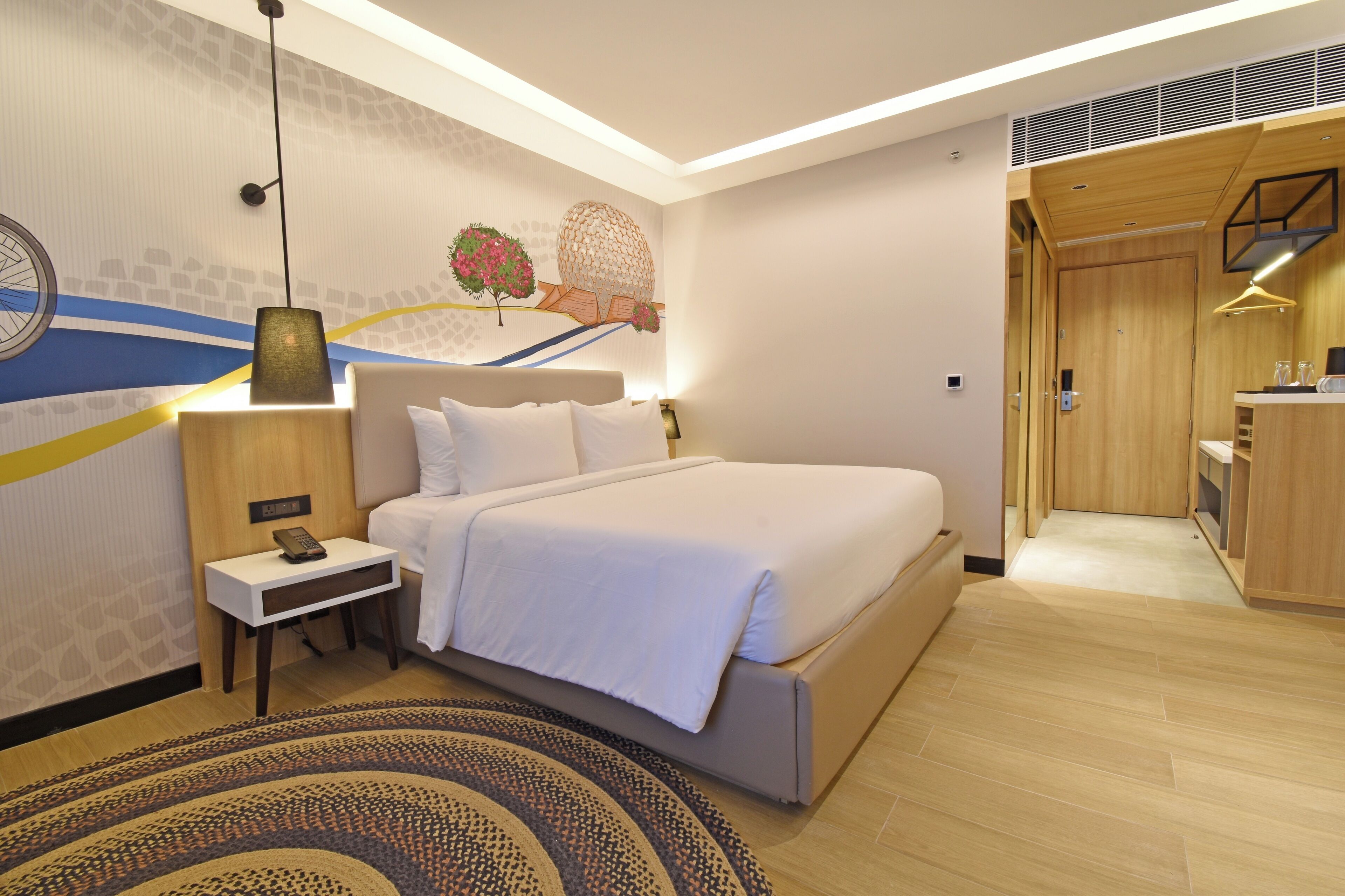 A modern hotel room with a large bed, bedside table, and a decorative wall mural.
