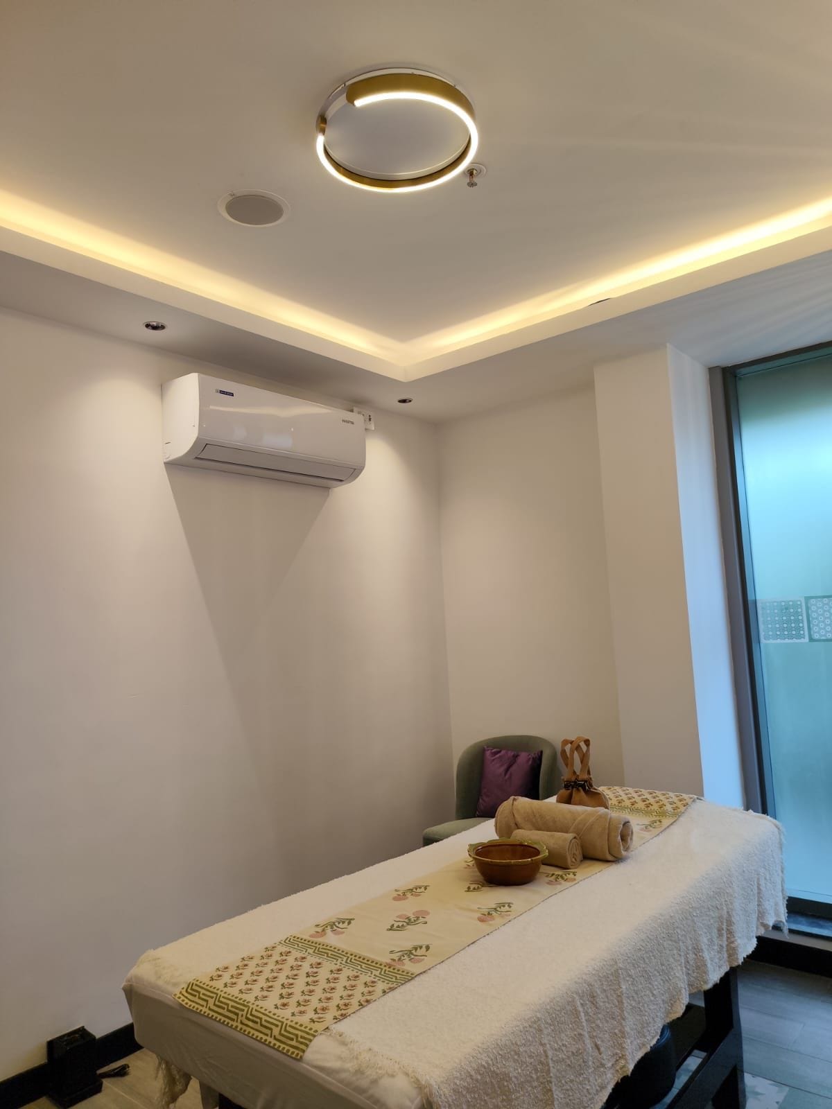 Una habitación con una mesa de masaje, un ventanal con vistas y un equipo de aire acondicionado.