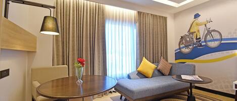 A modern hotel room with a sofa, a round table, a chair, and a decorative lamp.