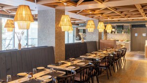 A restaurant with long communal tables, hanging rattan lamps, and a modern ceiling design. - Hotel Sands Point (Puducherry)