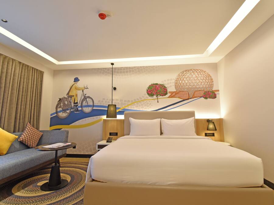 Een moderne hotelkamer met een groot bed, een bank, een eettafeltje en een decoratief muurschildering.
