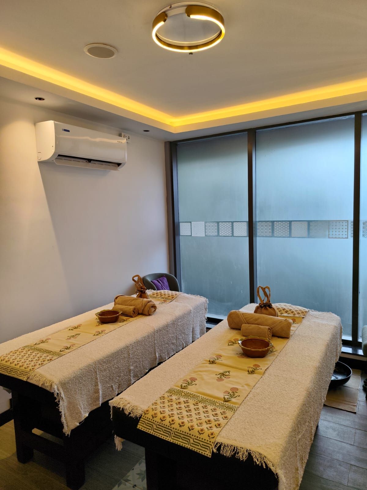 A room with two massage tables, each with towels and a bowl, and an air conditioning unit on the wall.