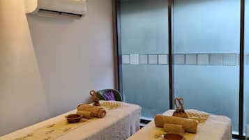 A room with two massage tables, each with towels and a bowl, and an air conditioning unit on the wall.