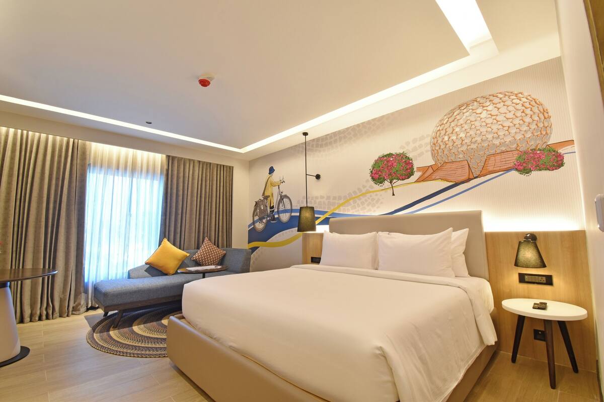 A hotel room with a large bed, a sofa, a small table, and a wall mural.