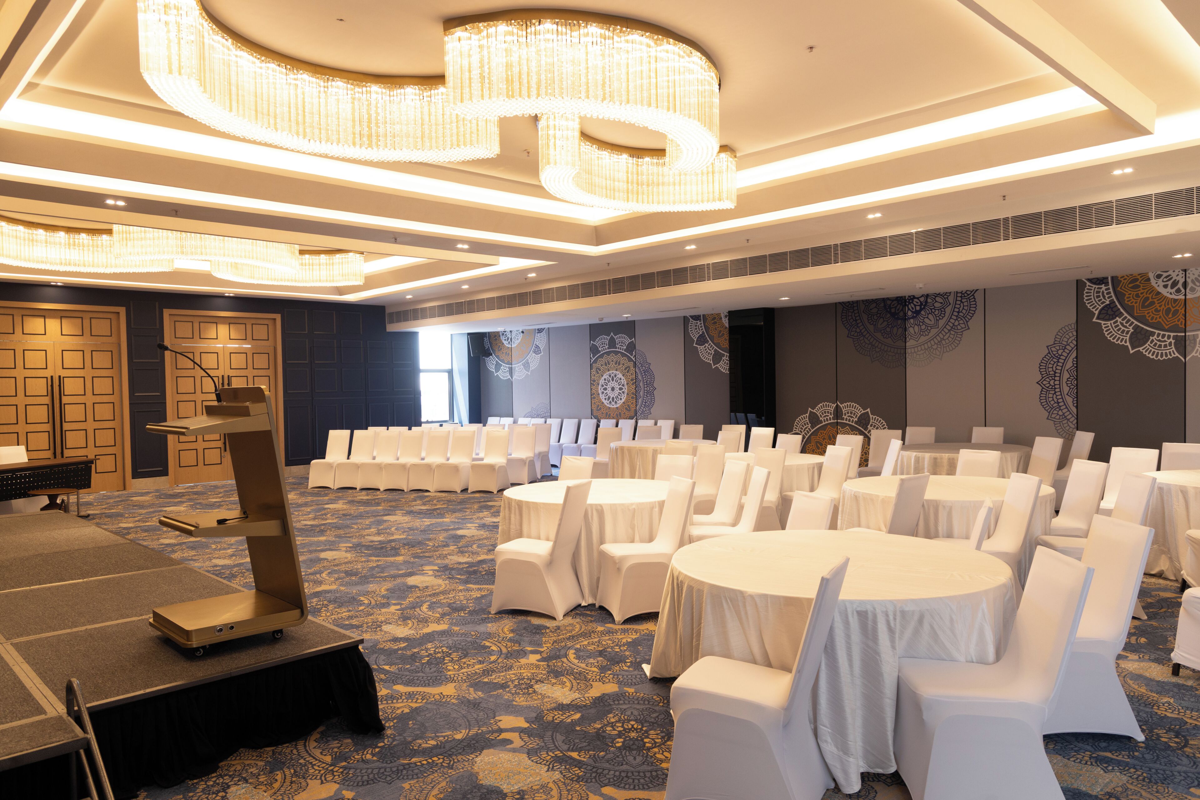 Une salle de banquet avec des tables rondes, des chaises blanches et un sol recouvert de moquette.
