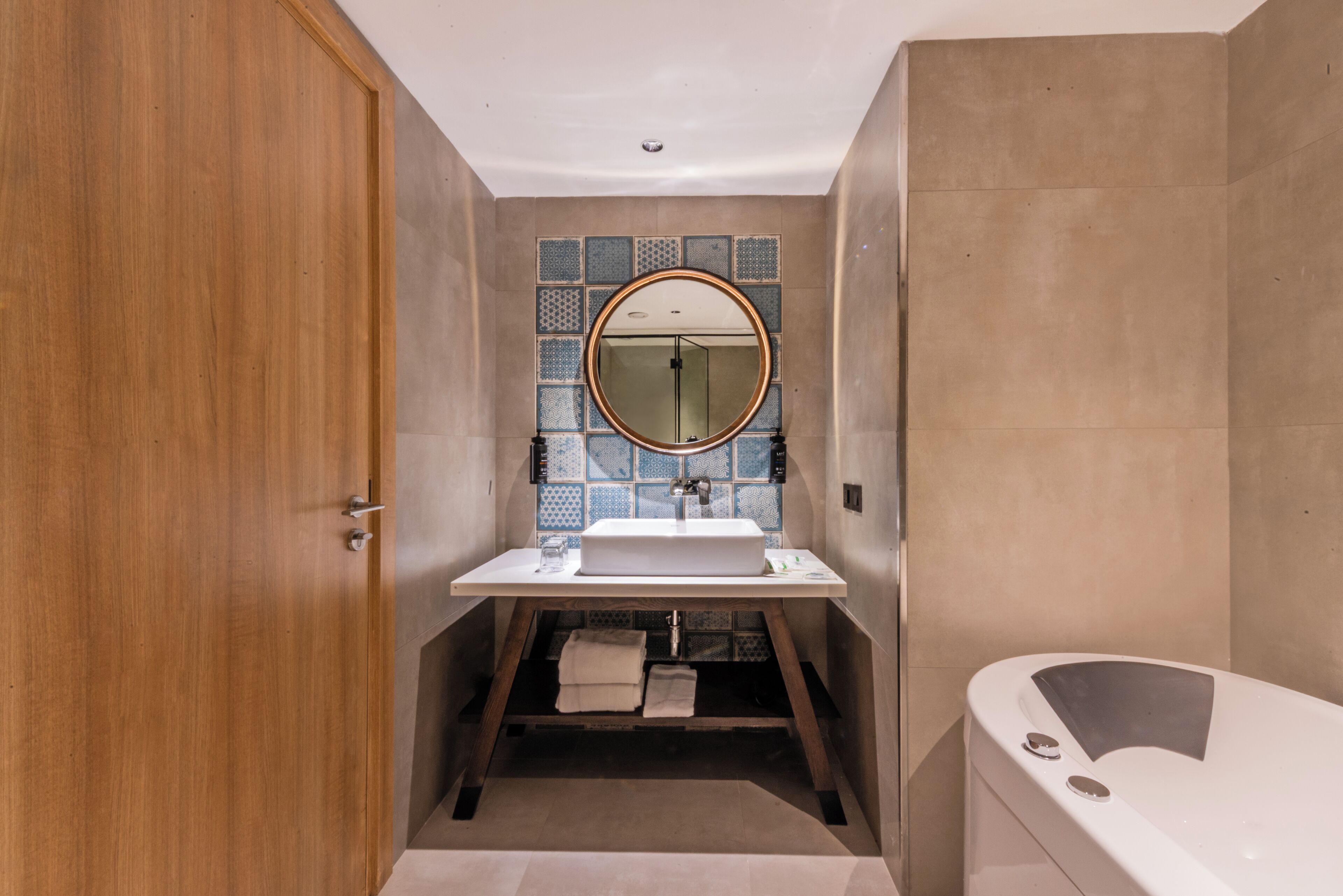 Une salle de bain avec une porte en bois, un lavabo avec un miroir, une baignoire et des murs carrelés.