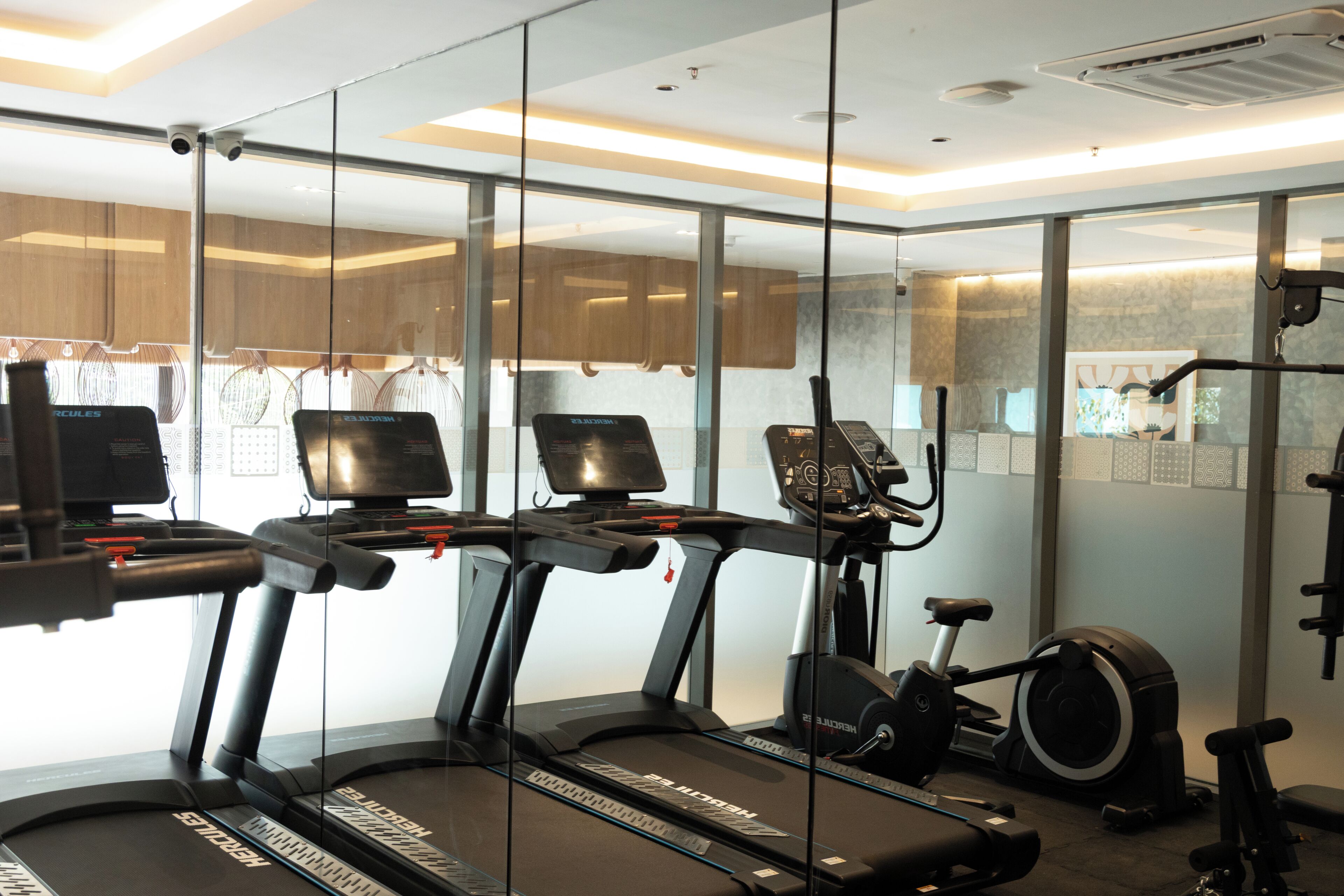 Un gimnasio con cintas de correr, elípticas y una bicicleta estática, con paredes de vidrio y un interior moderno.