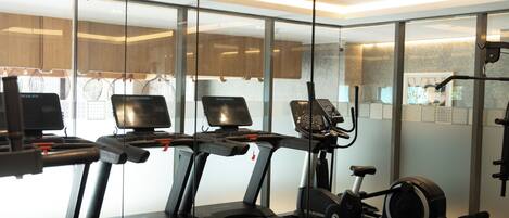 A gym with treadmills, an elliptical, and a stationary bike, with glass walls and a modern interior.