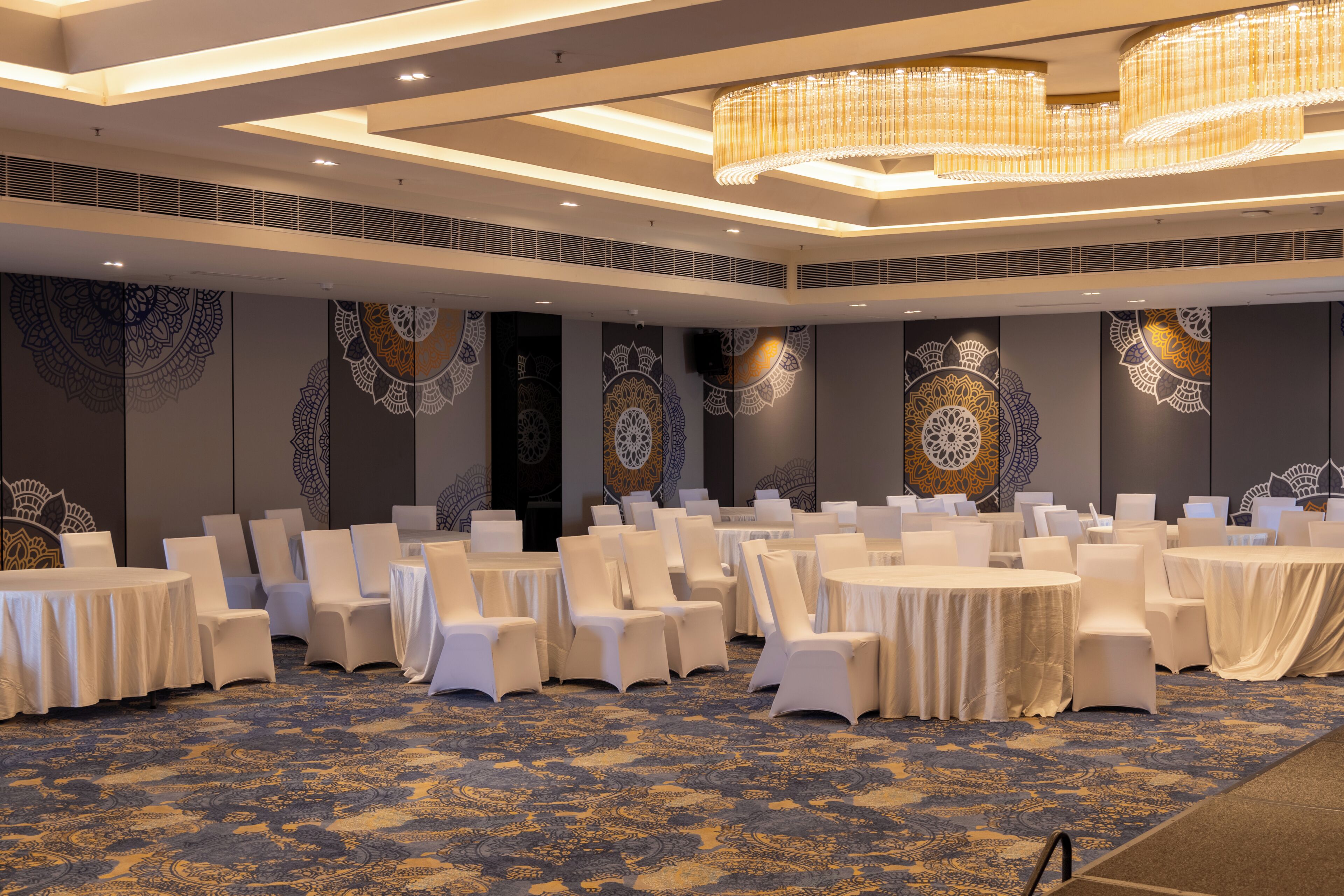 A banquet hall with round tables, white chairs, and patterned wall decorations.