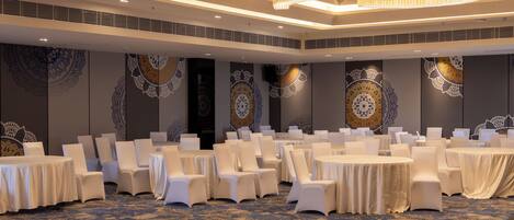 A banquet hall with round tables, white chairs, and patterned wall decorations.