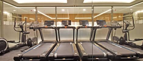 A gym with four treadmills, exercise bikes, and a mirrored wall.