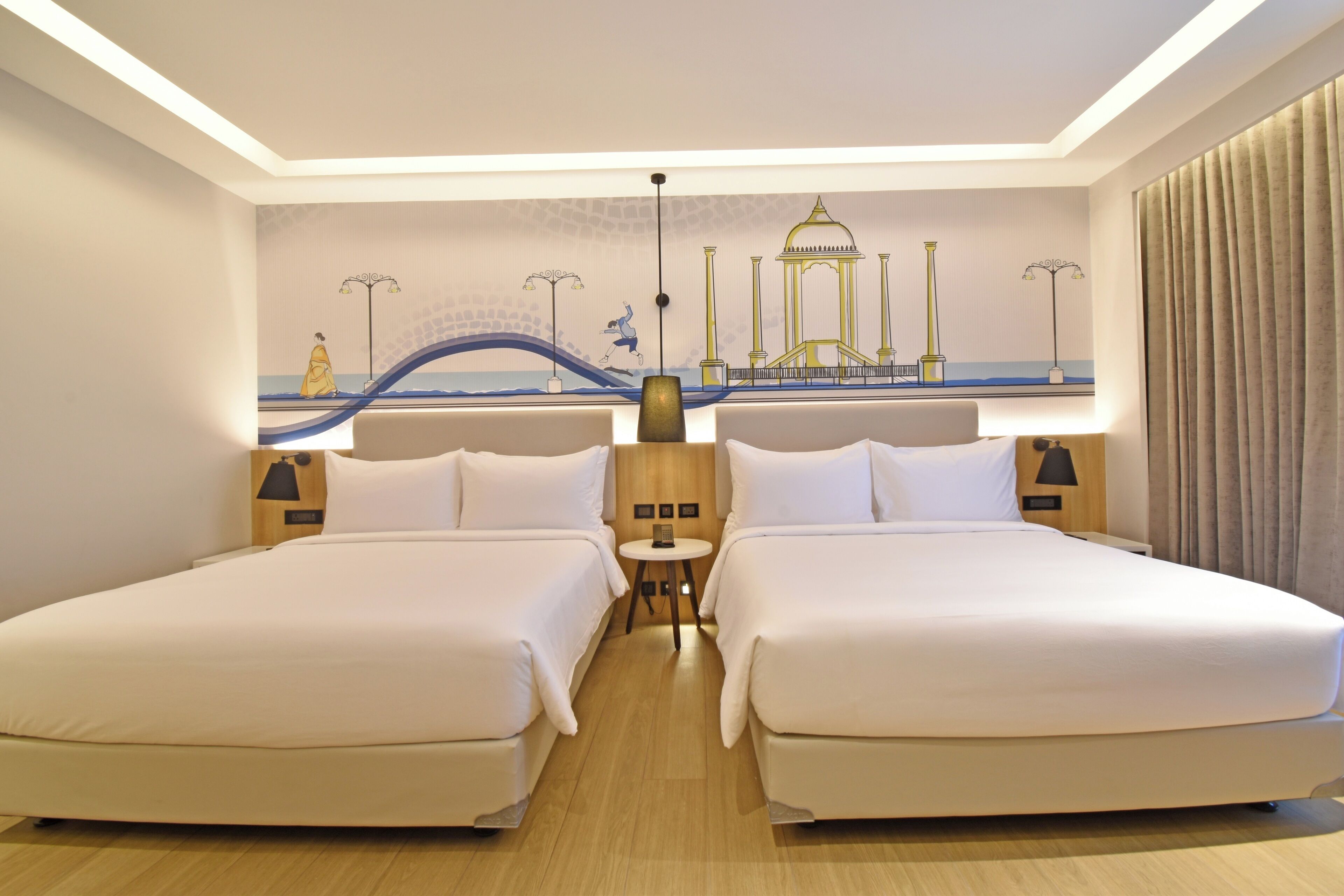 A hotel room with two beds, a small table, and a mural of a bridge and a building.