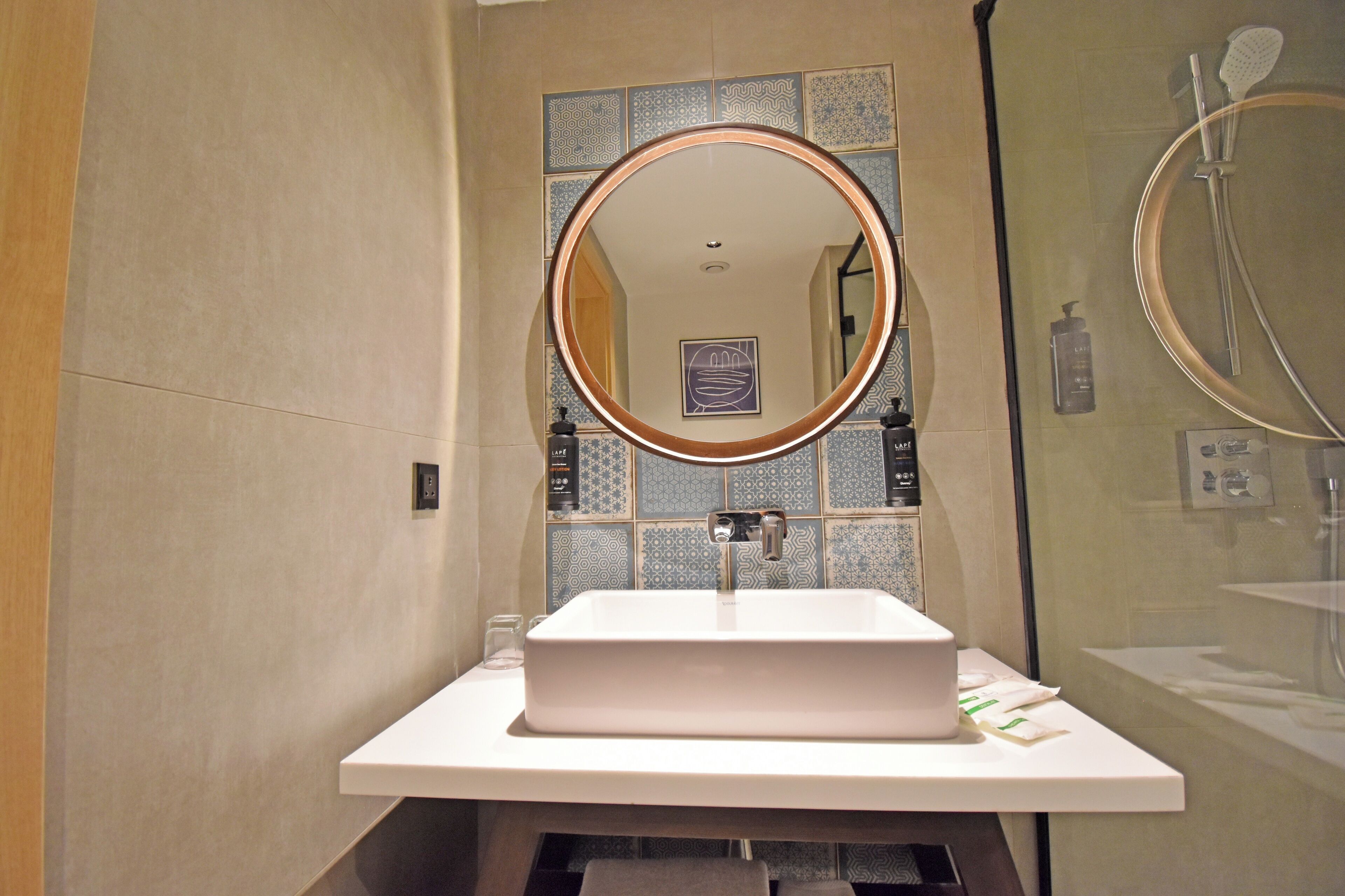 A bathroom with a rectangular sink, a round mirror, and a shower area.