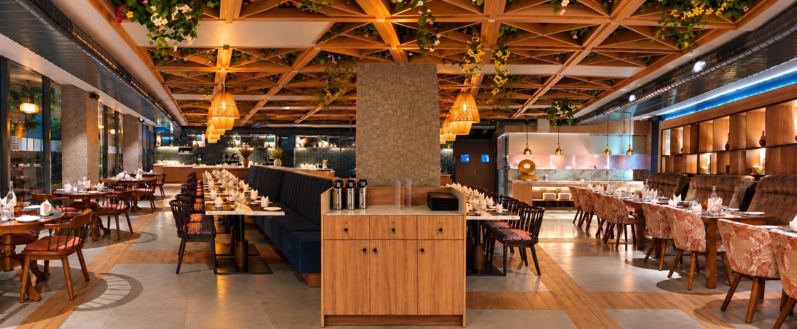 A restaurant with a long communal dining table, individual tables, and a bar area.