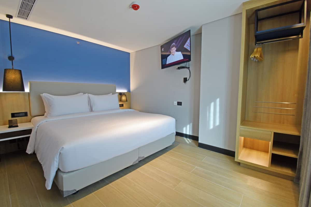 A modern hotel room with a large bed, a TV mounted on the wall, a bedside table, and a wooden wardrobe.