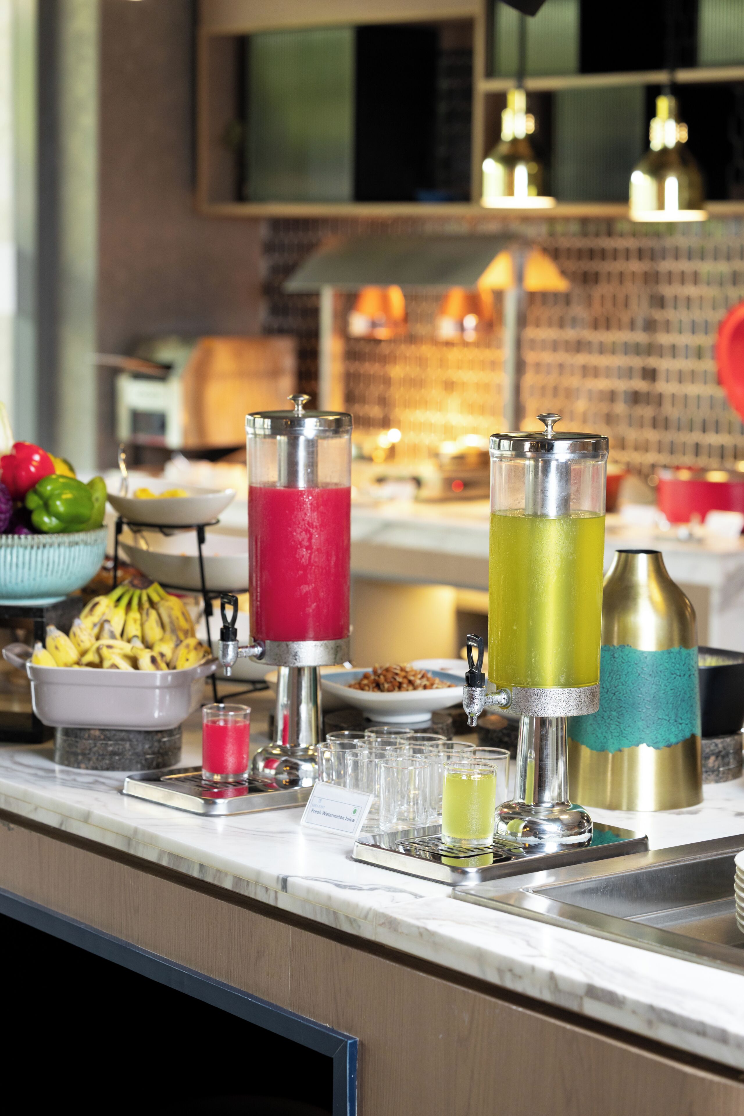 A bar area with a drink dispenser, a bowl of fruit, and a buffet setup.